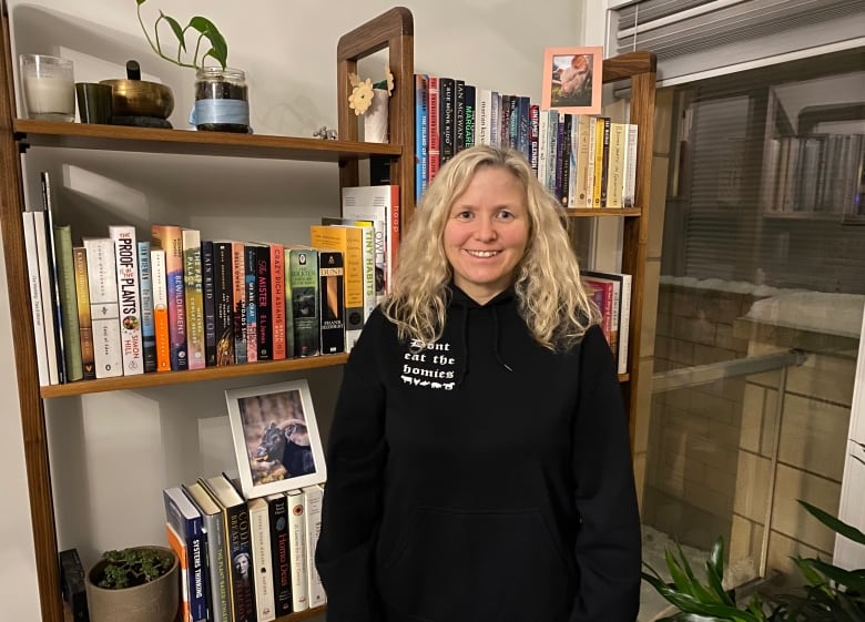 A woman stands in front of a book shelf.