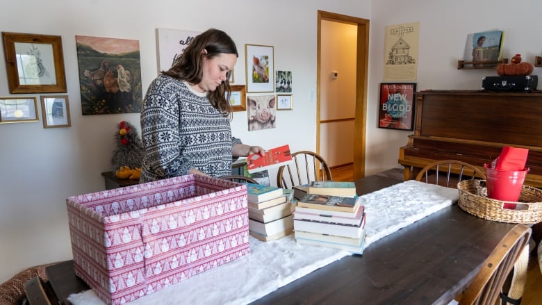 A woman looks at a book behind more books stacked up on table.