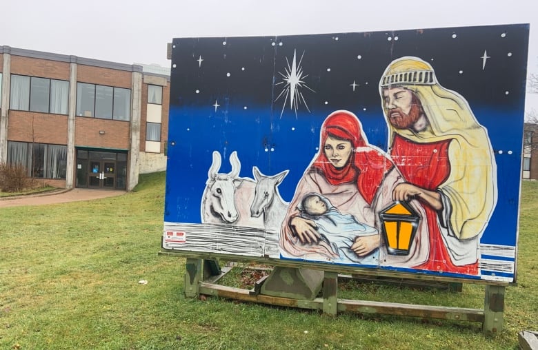 A painted nativity scene, featuring Mary, Joseph, baby Jesus and two farm animals, on a large sign outside a building.