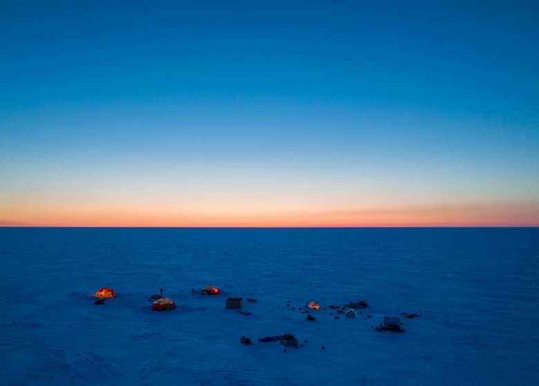 Glowing tents on deep blue ice, with a sunset sky. 