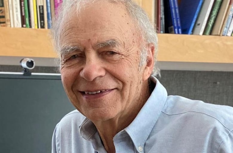 Professor in collared shirt, surrounded by books.