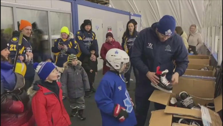 A man and children unpack boxes of hockey gear.