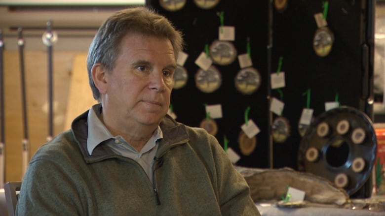 A man sits in front of a display board with wooden Christmas ornaments on it.