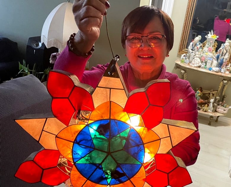 A woman holds up a stained-glass decoration. The star-shaped light has multiple stars— one red, one peach, one orange, and one green surrounded by a blue circle — shrinking in size from the outside in. 