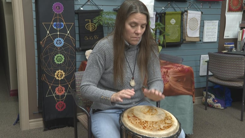 A woman sits playing a drum.