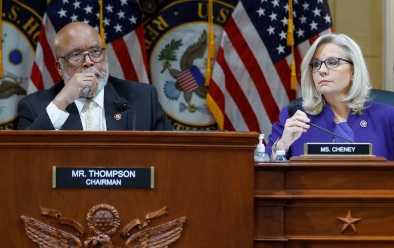 Two individuals sit behind the desk of the U.S. Congress. 