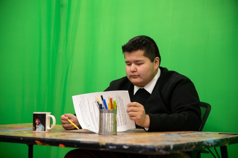 A young man flips through papers, reviewing a script. 