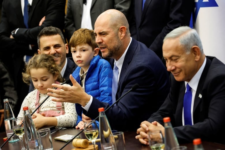 A bearded man sits with two children amid a group in the Israeli Parliament. 