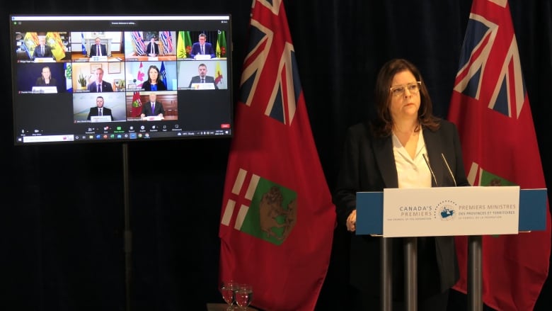 Heather Stefanson stands at a podium, in front of a monitor showing 10 other people in separate windows.