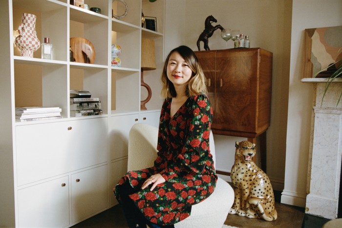 A smiling woman sits on cream-coloured fabric chair with a mahogany chest behind her and a porcelain leopard at her side