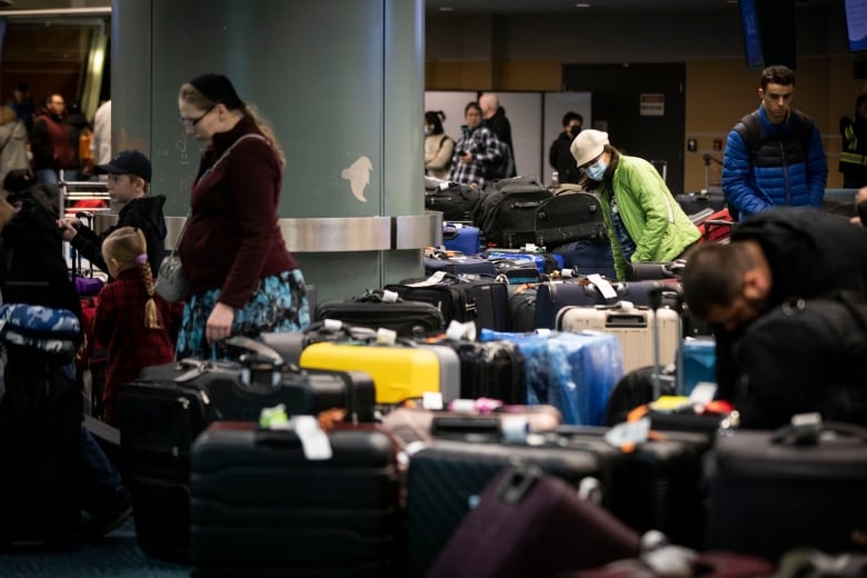 A passenger in a lime green sweater looks out at dozens of suitcases crowded at the baggage carousel at Vancouver International Airport.