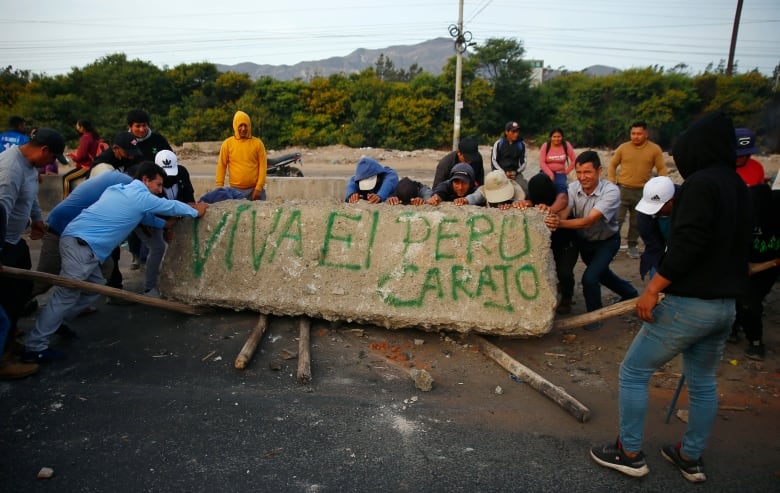 Protestors hold up a slab of concrete with the words 'Viva el Peru carajo' spray-painted on it in green.