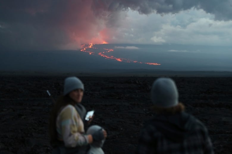 People in the forground taking a photo of the erupting vocano in the distance.