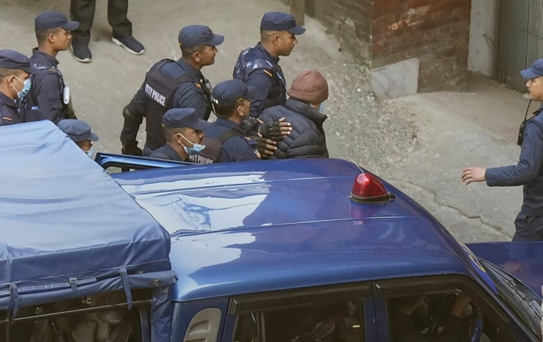 A man is escorted by police from a car.