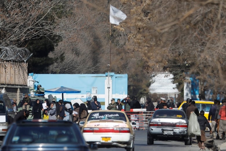 People stand in front of a building complex with a white flag.