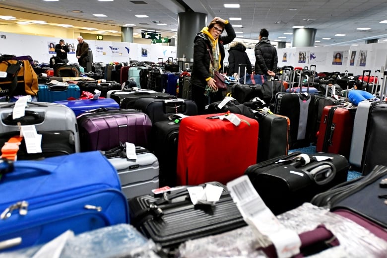 A person holds their head with their mouth agape as they look at a sea of suitcases.