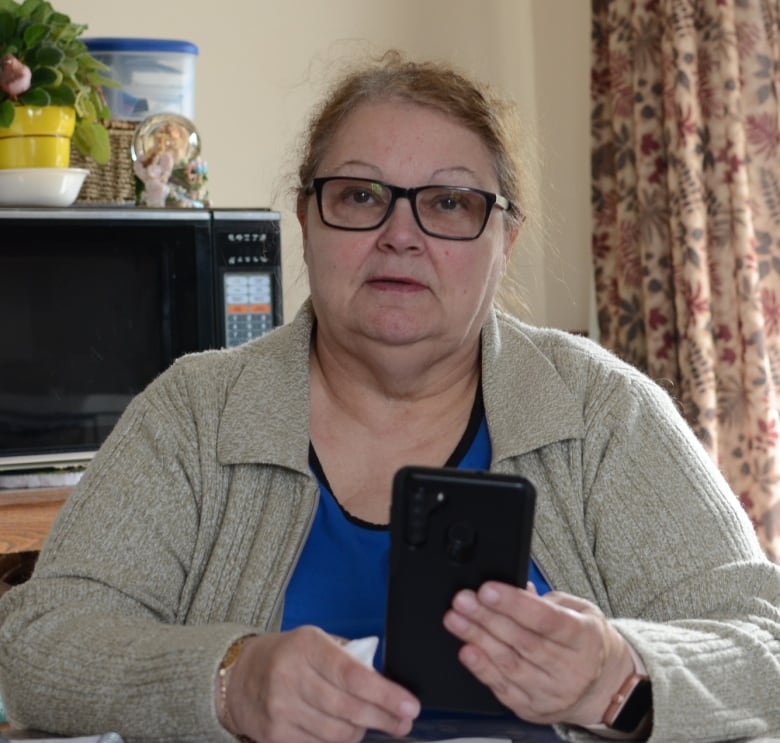 A woman sits at her kitchen table holding a smartphone. 