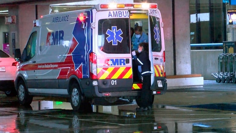 Two first responders are visible through the open back door of an ambulance parked outside a report.