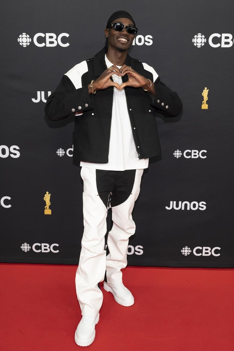 A man posing on the Junos red carpet wearing a black and white jacket, a white shirt, black and white pants, and all-white boots.  