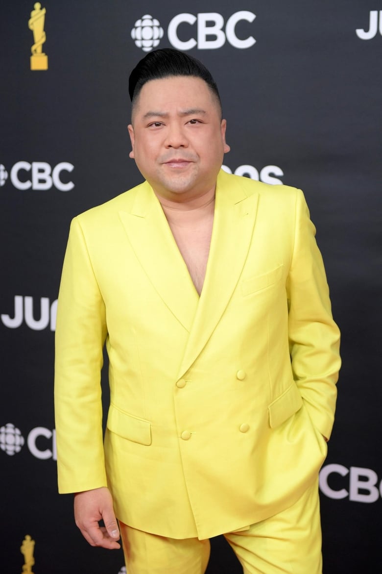 A man posing on the Junos red carpet wearing a yellow jacket and pants, and no shirt under the jacket. 