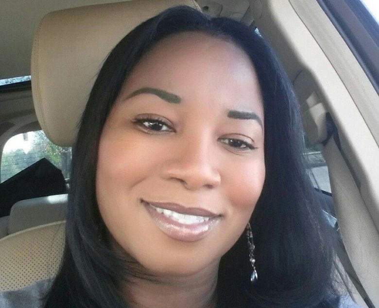 A Black woman with long dark hair smiles for a selfie while seated in a car.