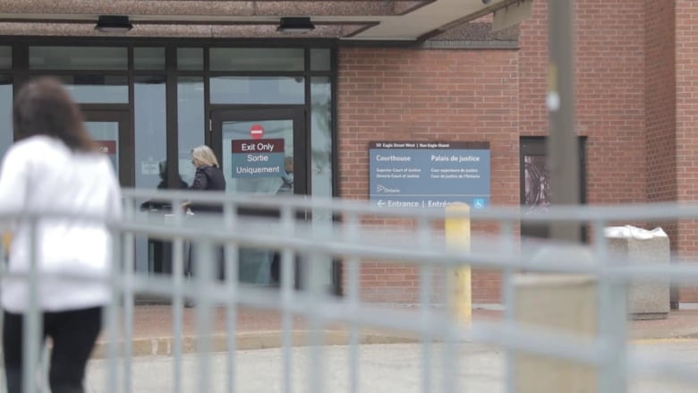 The exterior of a red brick courthouse and a pair of glass doors is shown, with two people passing by. 