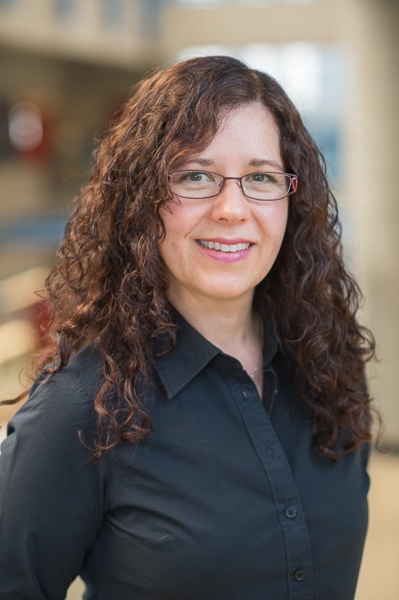 A woman with long, brown hair and glasses looks directly at the camera.