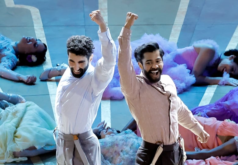 Two dancers perform on stage, with backup dancers arrayed behind them on the floor.