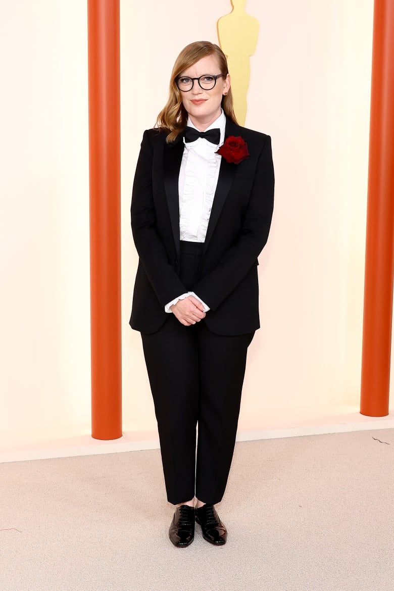 A woman wears a tuxedo with a rose attached to the lapel.