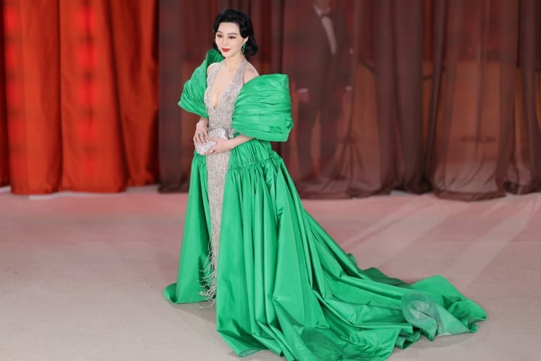 A woman wears a sparkling silver gown with a bright green coat.