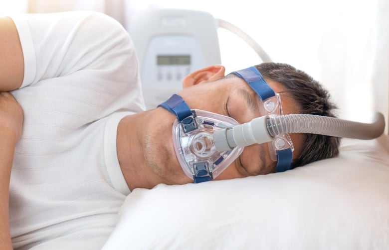 Man sleeping in bed on his side hooked up to a CPAP machine.