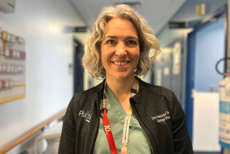 A woman dressed in medical scrubs smiles into the camera in a hospital hallway.