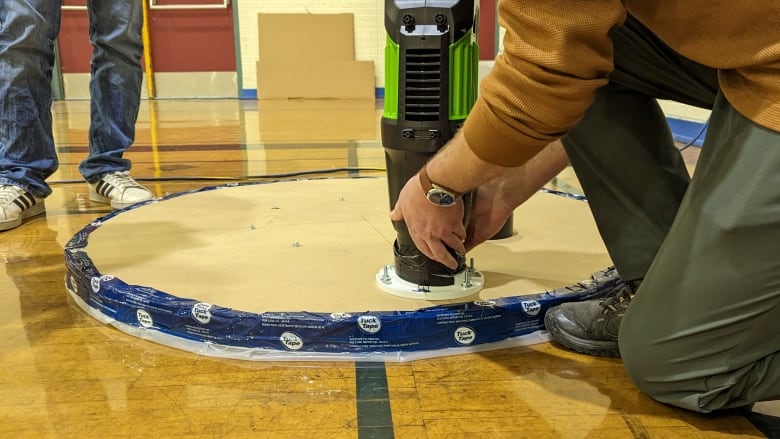 A person huddles over a hovercraft placing a leaf blower into it