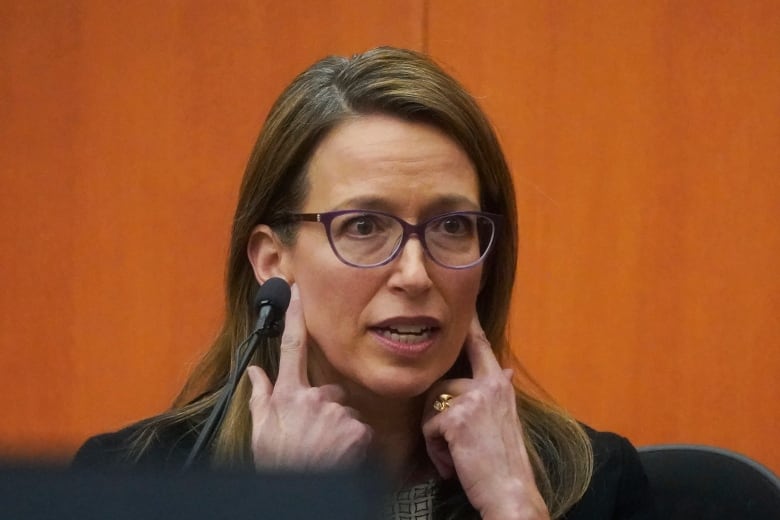 A woman points at her ears in a courtroom.