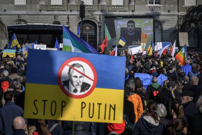 Protestors hold a yellow and blue banner saying ‘Stop Putin’ 