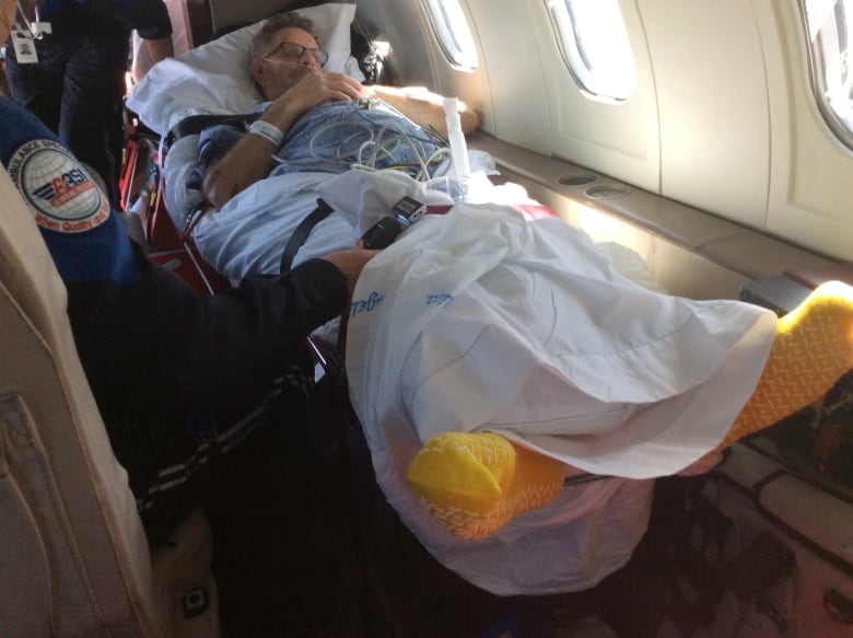 A man lies on a stretcher on an airplane