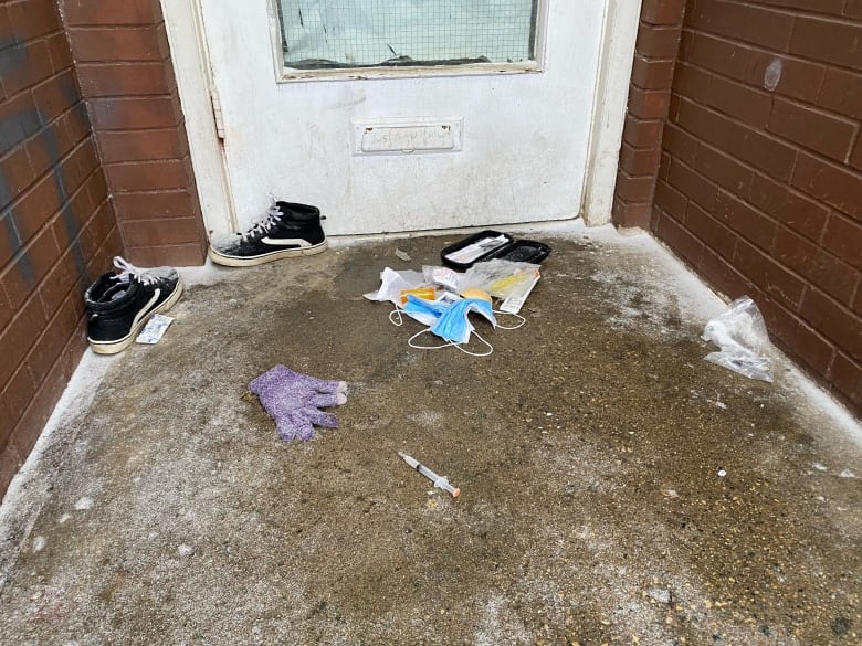 A pair of sneakers, a syringe and naloxone kit in front of a doorway.  