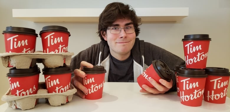 A man poses next to many, many Time Hortons coffee cups.