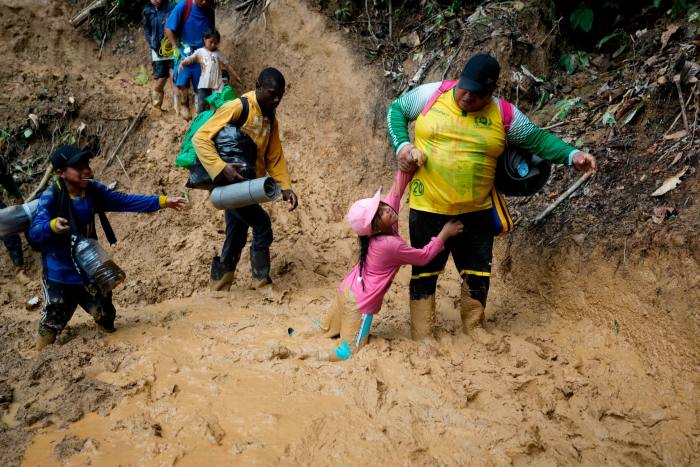 A woman lifts a child from a muddied path as migrants walk across the Darién Gap