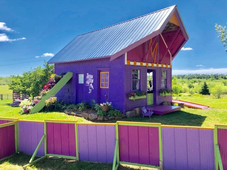 A bright purple and green building, on a sunny day in a green rural area.