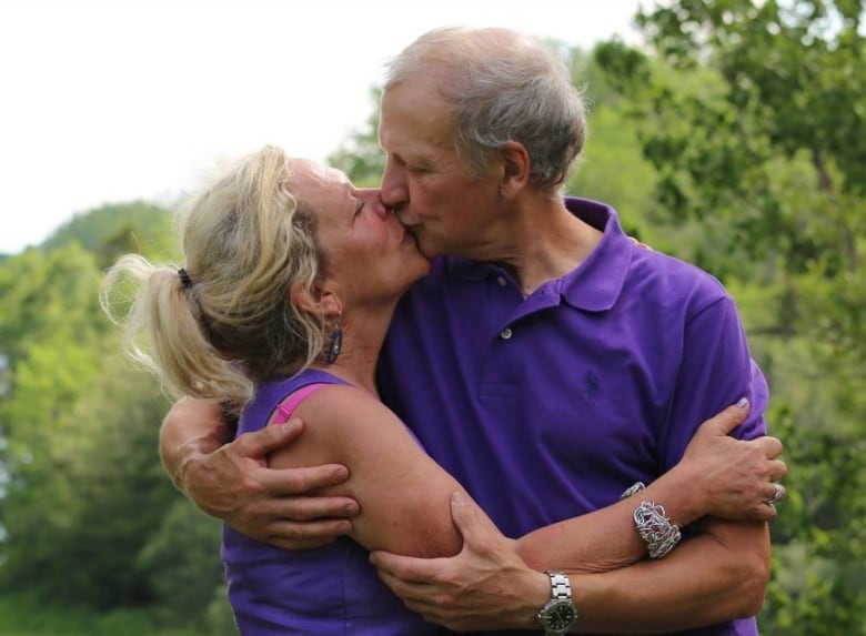 A man and woman stand outside, kissing. 