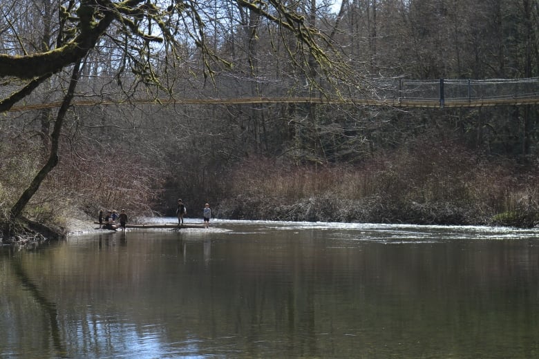 An idyllic shot of a peaceful river with water as smooth as glass shows two people on its edge in the distance.