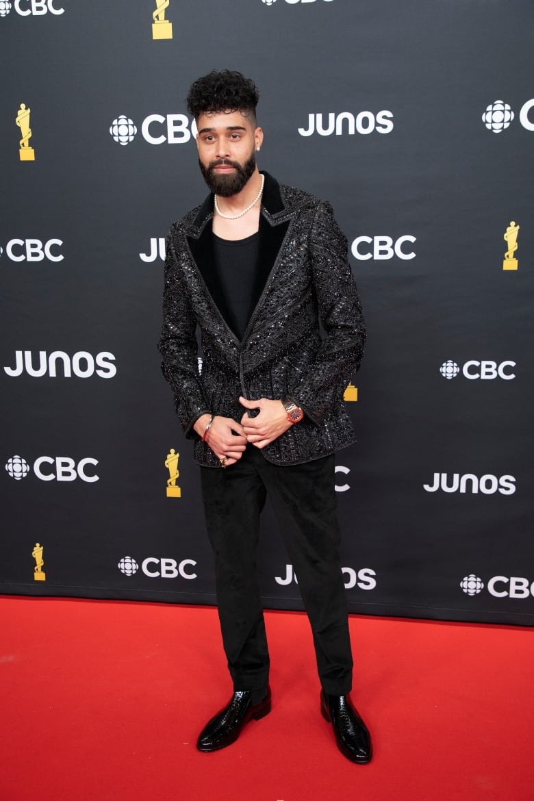 Man in shiny black suit posing on red carpet.