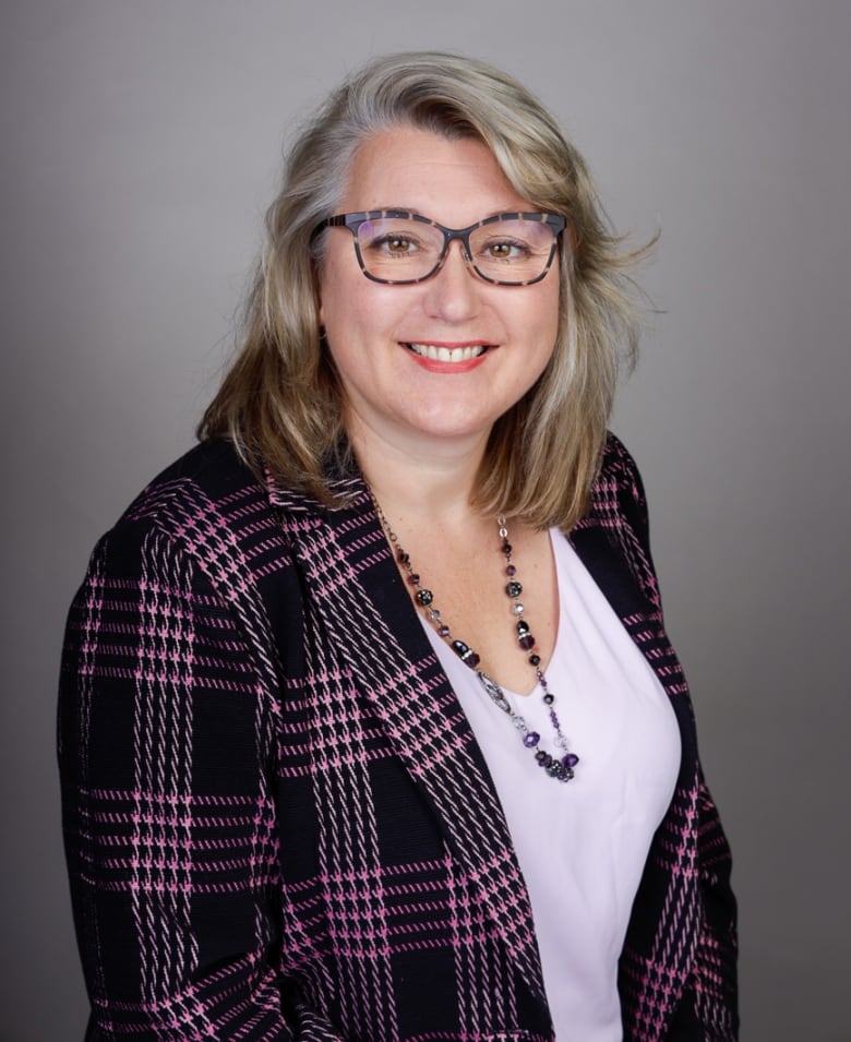 A woman with glasses and a black and purple plaid blazer poses for a portrait.