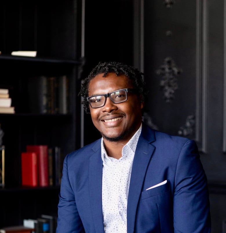 A man in a blue suit with a white shirt and glasses.