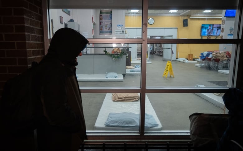 A man wearing a hooded winter jacket stands outside a shelter.