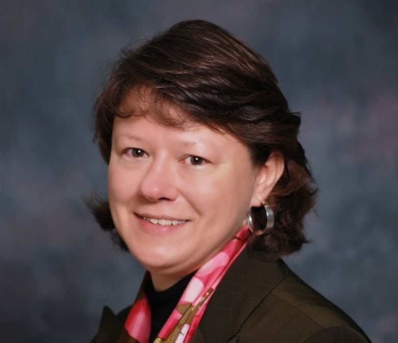 Woman with dark brown hair, wearing a pink-patterned scarf, poses in front of a grey backdrop.