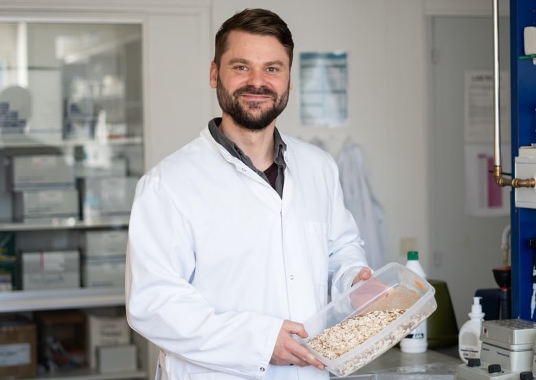 Man in white lab coat holding up a container of insect larvae.