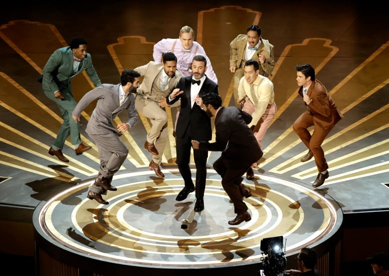 Man on a stage surrounded by dancers