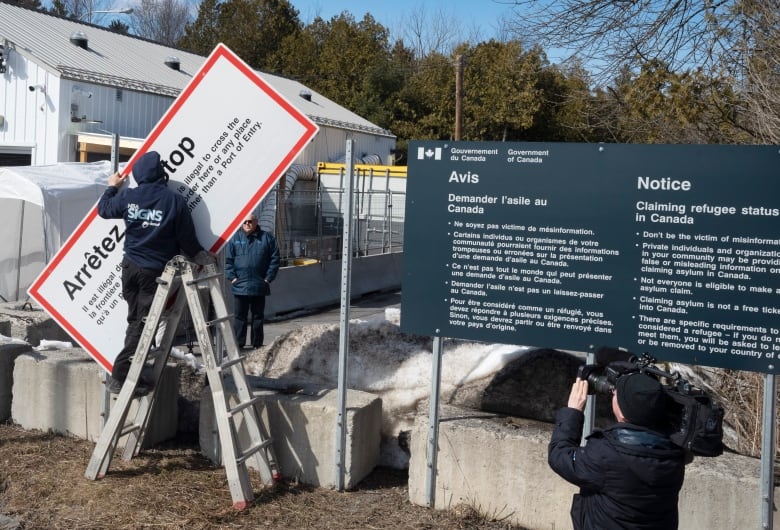 Workers remove current warning signs at the irregular border at Roxham Road from New York into Canada on Friday, March 24, 2023.